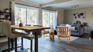 Amplia sala de estar con mesa de comedor de madera, asientos acolchados y un sofá gris.