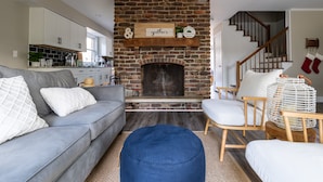 Una sala de estar con chimenea de piedra, un sofá gris y una silla de madera.