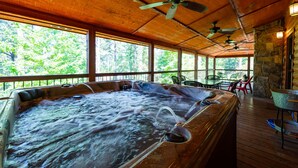 Ein Whirlpoolbereich mit Holzboden, Steinwänden und Blick auf Bäume durch große Fenster.