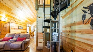 Ein gemütliches Blockhaus-Interieur mit Holzboden, einer Couch mit roten Kissen, einer dekorativen Eule und einer Metalltrichter-Konstruktion.