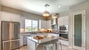 A modern kitchen with stainless steel appliances, a large island, and pendant lighting. - Brand New Desert Princess Villa with Private Pool, Spa and View (Cathedral City)