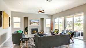 A spacious living room with a fireplace, grey sofas, a coffee table, and a large sliding glass door leading to an outdoor patio. - Brand New Desert Princess Villa with Private Pool, Spa and View (Cathedral City)