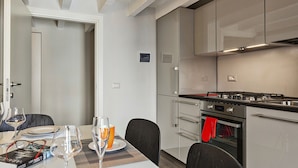 A modern kitchen with stainless steel appliances, a dining area with a table set for two, and a door leading to another room. - Boutique Apartment in Via Roma by Wonderful Italy (Genova)