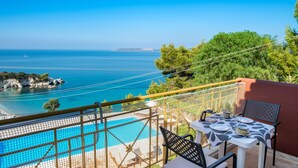 A poolside area with a table and chairs, overlooking a clear blue sea and a rocky coastline. - Private Villas with Shared pool#1 (Argostoli)