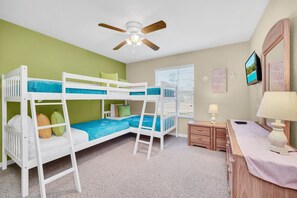A bunk bed room with a ceiling fan, a small bedside table, a lamp, and a TV on the wall.