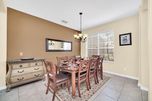 A dining room with a wooden table set for four, surrounded by chairs, a chandelier, and a decorative mirror on the wall.
