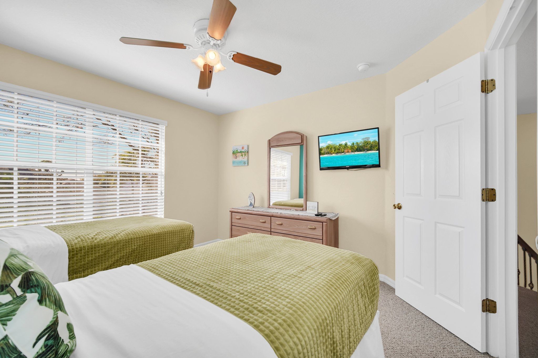 A bedroom with two beds, a ceiling fan, a television, and a door.