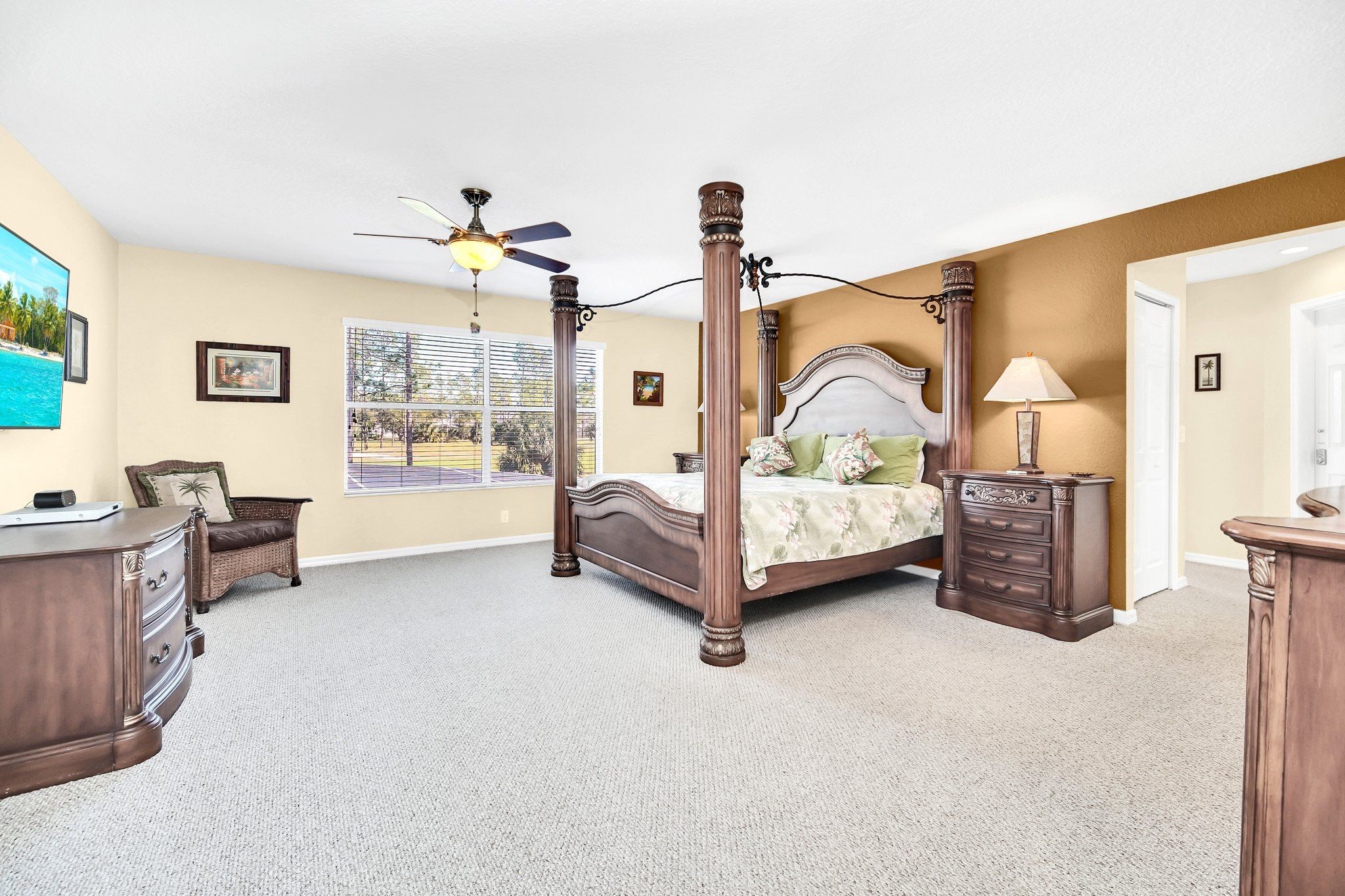 A bedroom with a four-poster bed, a ceiling fan, a desk, and a chair.