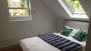 A bedroom with a sloped ceiling, a skylight, a bed with white bedding, a blue blanket, and green leaf-patterned pillows. - Self Contained Coach House (Bromley)