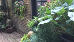 A brick building with a black door, potted plants, and hanging vines. - Self Contained Coach House (Bromley)