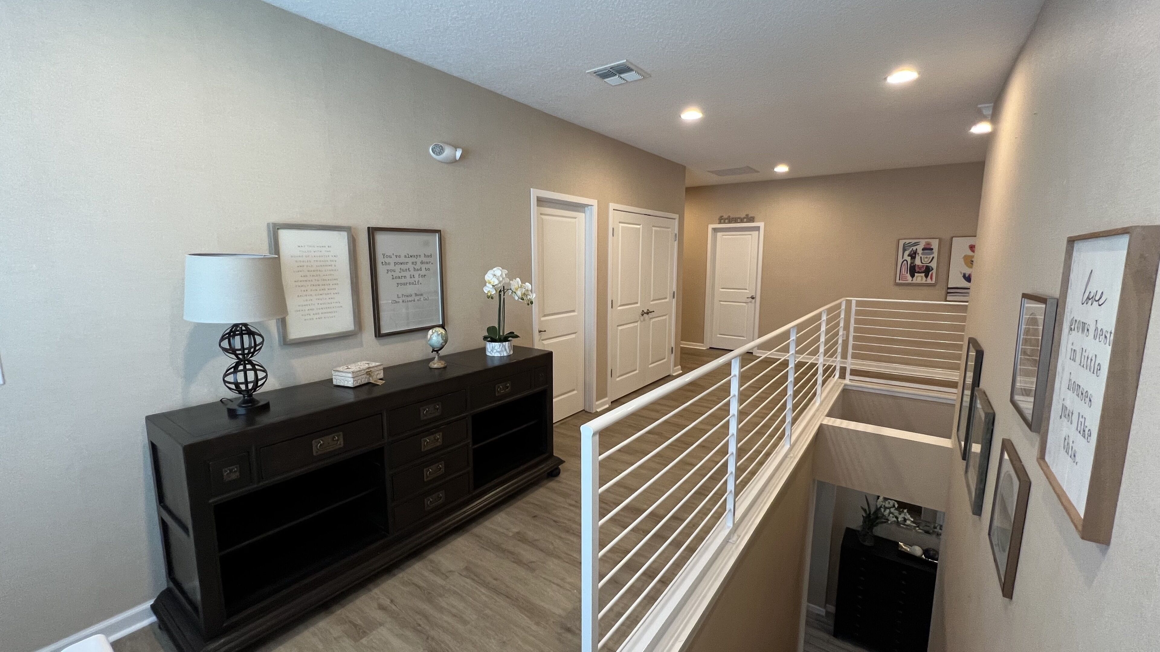 A modern interior with a staircase, a dark wooden console, framed quotes, and a white railing.