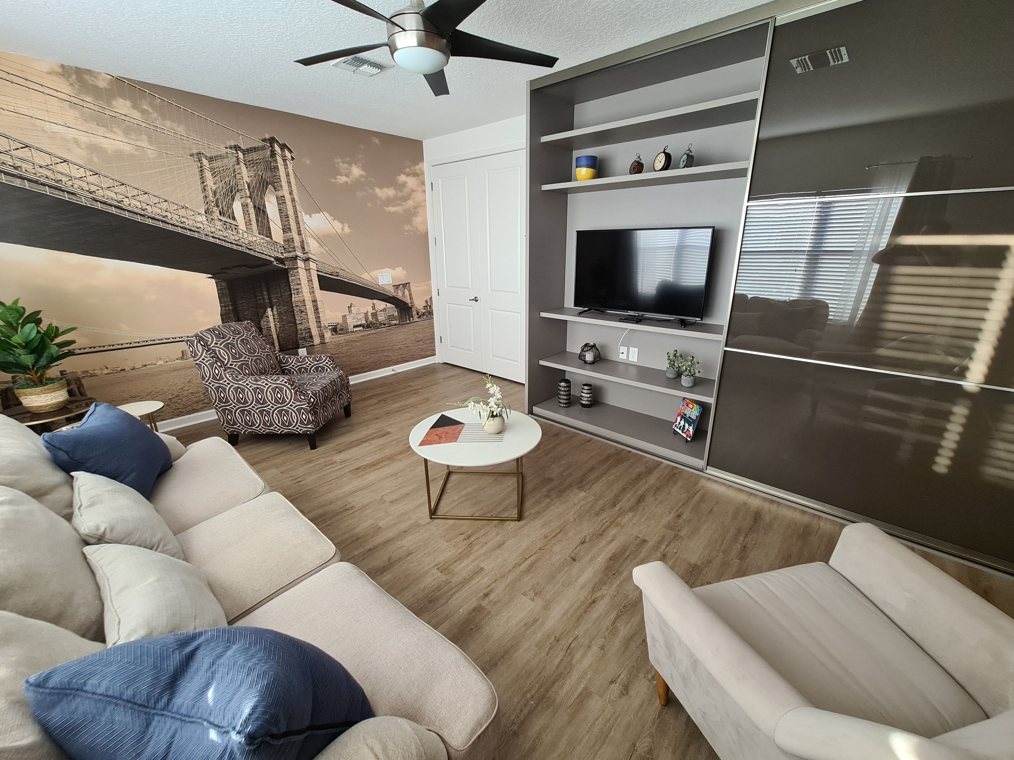 A modern living room with a large TV, a sofa, a patterned armchair, and a coffee table.