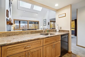 A kitchen with granite countertops, wooden cabinets, a dishwasher, and a window with a view of trees. - 2-bedroom plus loft condo with mountain views, pool, and hot tub. (Killington)