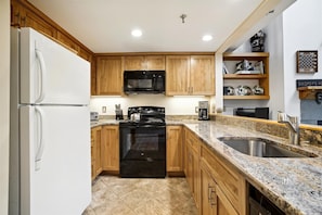 A kitchen with wooden cabinets, a black microwave, a stove, a sink, and a refrigerator. - 2-bedroom plus loft condo with mountain views, pool, and hot tub. (Killington)