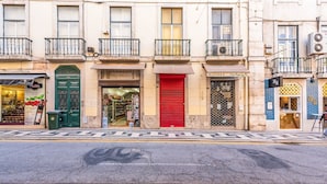 A street view with a row of shops, including a bakery and a deli, with a red shutter door and a green door. - GuestReady - Groovy Fanqueiros (Lisbon)
