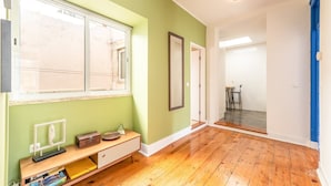 A spacious hallway with wooden flooring, a large window, and a bench with books. - GuestReady - Groovy Fanqueiros (Lisbon)