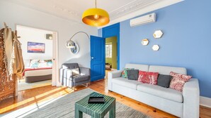 A modern living room with a blue accent wall, a grey sofa, a wooden coffee table, and a yellow pendant light. - GuestReady - Groovy Fanqueiros (Lisbon)
