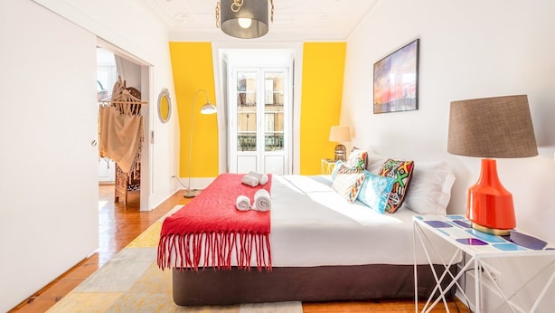 A hotel room with a bed, a nightstand, a lamp, a window, and a door. - GuestReady - Groovy Fanqueiros (Lisbon)