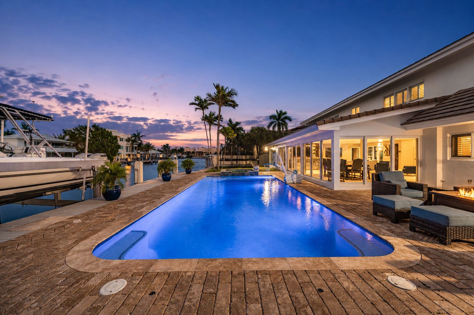 A swimming pool with a wooden deck, palm trees, and a building with outdoor seating.