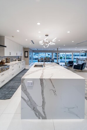 A modern kitchen with a large island, white cabinetry, and a view to the outside. - Luxurious, Modern Fort Lauderdale House with Waterfront Pool & Spa (Fort Lauderdale)