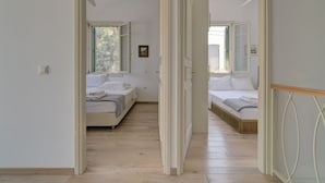 A corridor leading to two bedrooms with wooden flooring, white walls, and ceiling fans.