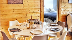 A wooden interior with a dining table set for four, glasses, plates, and a bottle of champagne. - La Ménandière - 3 bedrooms (Megève)
