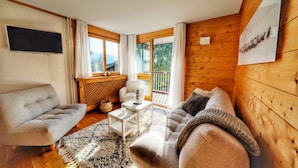 A modern living room with a sofa, armchair, and coffee table. There is a TV mounted on the wall and a window with curtains. - La Ménandière - 3 bedrooms (Megève)