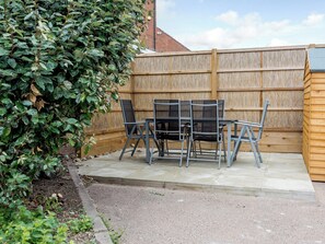 A patio area with a table and chairs, a wooden fence, and a hedge.