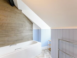 A modern bathroom with a wooden wall, a white bathtub, and a blue accent wall.
