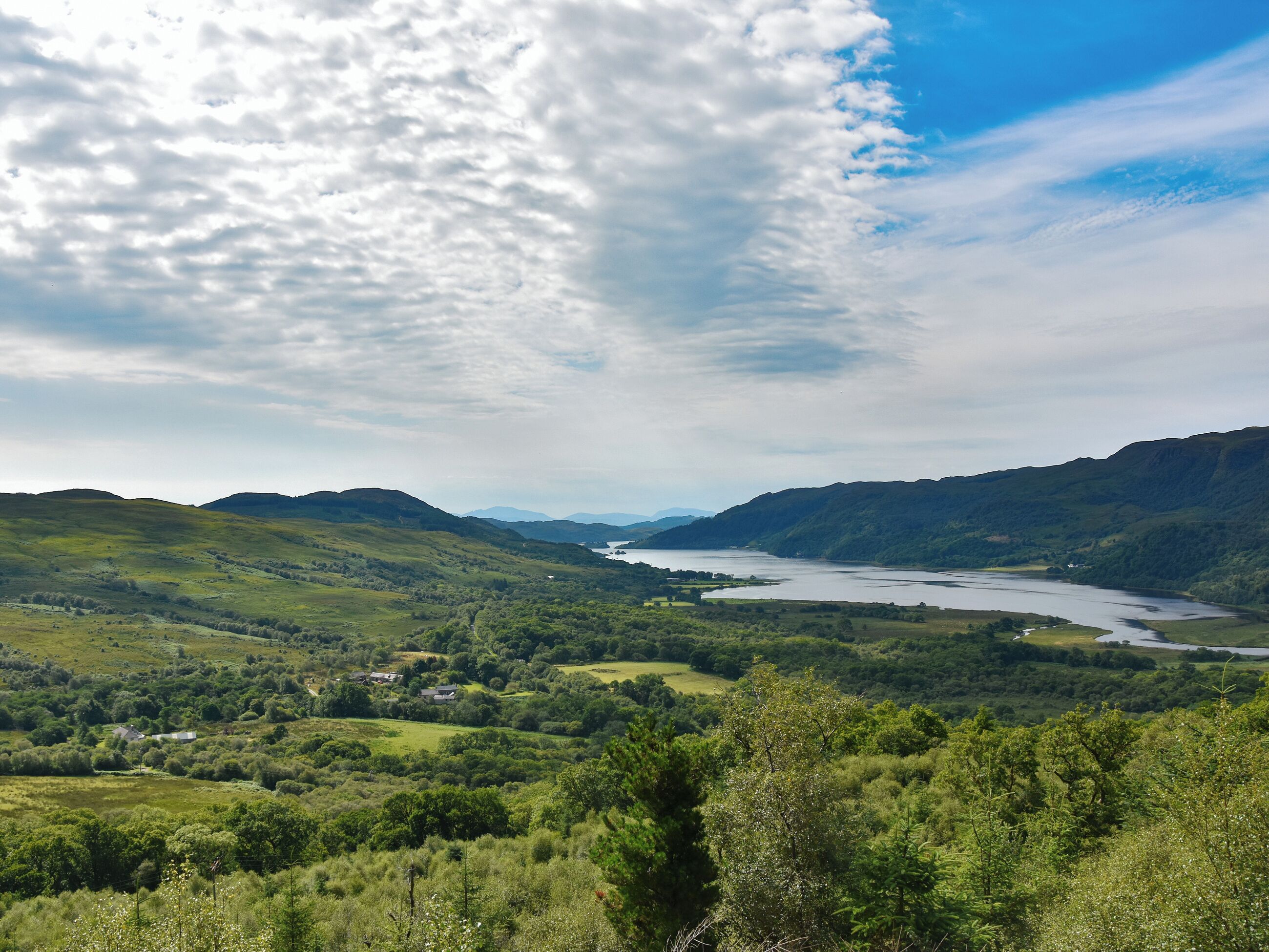 A panoramic view of a valley with a river, hills, and scattered buildings.
