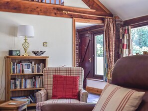 A cozy living room with a plaid armchair, a bookshelf, and a wooden ceiling.