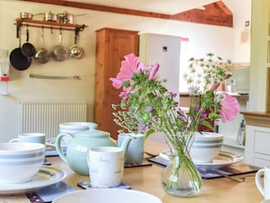 A kitchen with a wooden cabinet, hanging pots, and a vase with flowers on the counter.