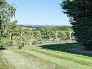 Un paysage verdoyant avec une structure de pergola en bois, des arbres et une vue lointaine sur des champs.