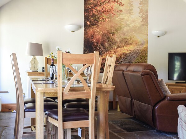 Un coin repas avec des chaises en bois, une table à manger et un grand tableau représentant une scène de forêt.
