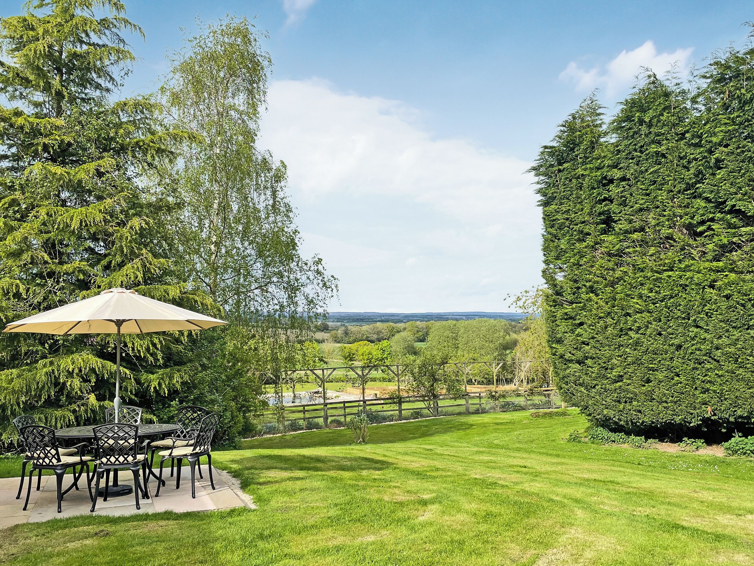 Eine Terrasse mit Tisch und Stühlen, einem großen Sonnenschirm und einem gepflegten Rasen.