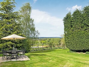 Eine Terrasse mit Tisch und Stühlen, einem großen Sonnenschirm und einem gepflegten Rasen.