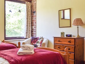 Ein Schlafzimmer mit zwei Betten, einer Holzkombination, einem Nachttisch, einer Lampe, einem Spiegel und einem Fenster mit Vorhängen.