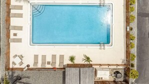 Eine Vogelperspektive auf einen rechteckigen Swimmingpool mit Fliesen umgeben von Liegestühlen und kleinen Pflanzen.