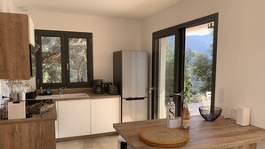 A modern kitchen with a wooden countertop, a built-in coffee maker, and a view of the outdoors through large windows. - Villa PETRU **** with swimming pool, sea view, 10 mn from the beach (Sari-d'Orcino)