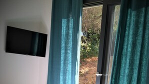 A bedroom with a bed, a TV mounted on the wall, and a view of the outdoors through a door with curtains. - Villa PETRU **** with swimming pool, sea view, 10 mn from the beach (Sari-d'Orcino)