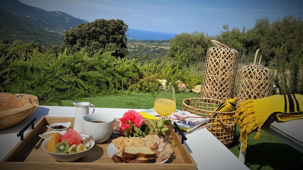 A table set with food and drinks, overlooking a scenic landscape with mountains and greenery. - Villa PETRU **** with swimming pool, sea view, 10 mn from the beach (Sari-d'Orcino)