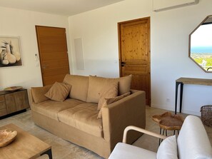 A living room with a beige sofa, wooden doors, a small table, and a view through a window.