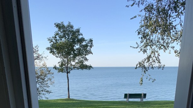 A view from a door to a deck overlooking a grassy area with a bench and a tree. - Enjoy the View From this Charming Lakefront House in Private Park (Huron)