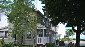 A two-story house with a porch, surrounded by a garden with various plants and a tree. - Enjoy the View From this Charming Lakefront House in Private Park (Huron)