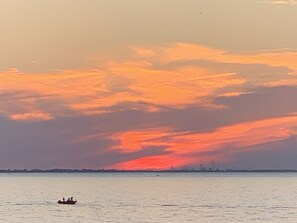 A sunset over a calm body of water with a distant city skyline. - Enjoy the View From this Charming Lakefront House in Private Park (Huron)