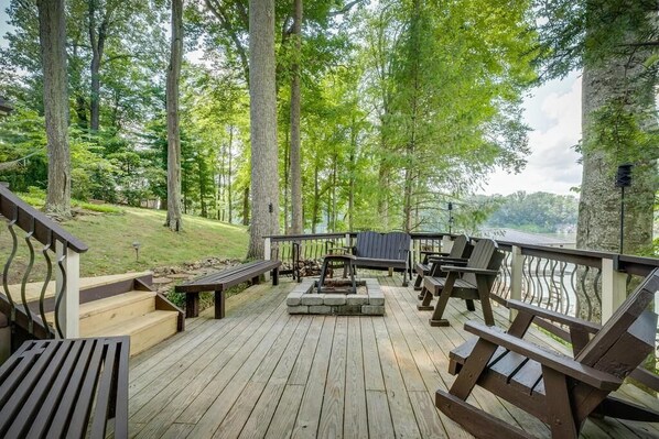 A wooden deck with outdoor seating, a fire pit, and a view of a forested area.