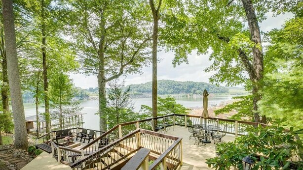 A deck with outdoor seating overlooking a lake, surrounded by trees.