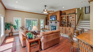 A spacious living room with a fireplace, a dining area with a wooden table and chairs, and a kitchen with wooden cabinets and a TV.