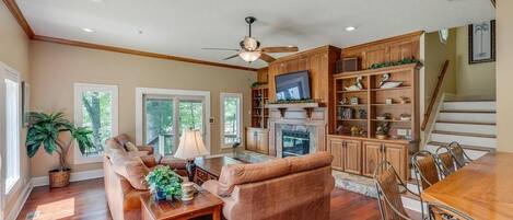 A spacious living room with a fireplace, a dining area with a wooden table and chairs, and a kitchen with wooden cabinets and a TV.