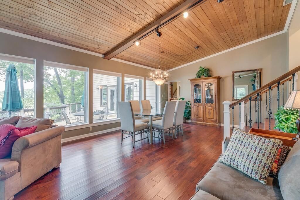A spacious living room with hardwood floors, a dining area with a chandelier, and a staircase with a wooden railing.
